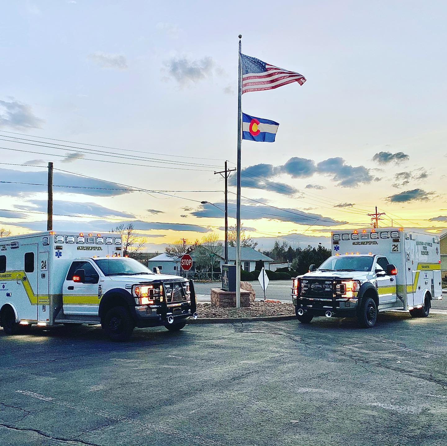 Two ambulances parked next to a flagpole with the American and Colorado flags